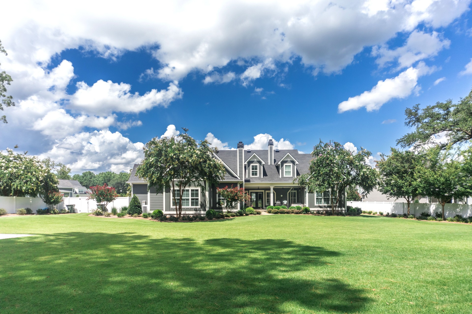 The side view of the backyard of a large gray craftsman new construction house with a landscaped yard